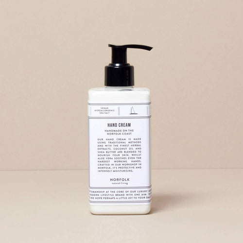 A bottle of Norfolk Natural Living Coastal Hand Lotion with a pump dispenser on a beige background. The label includes text describing the product's moisturizing features and origin.