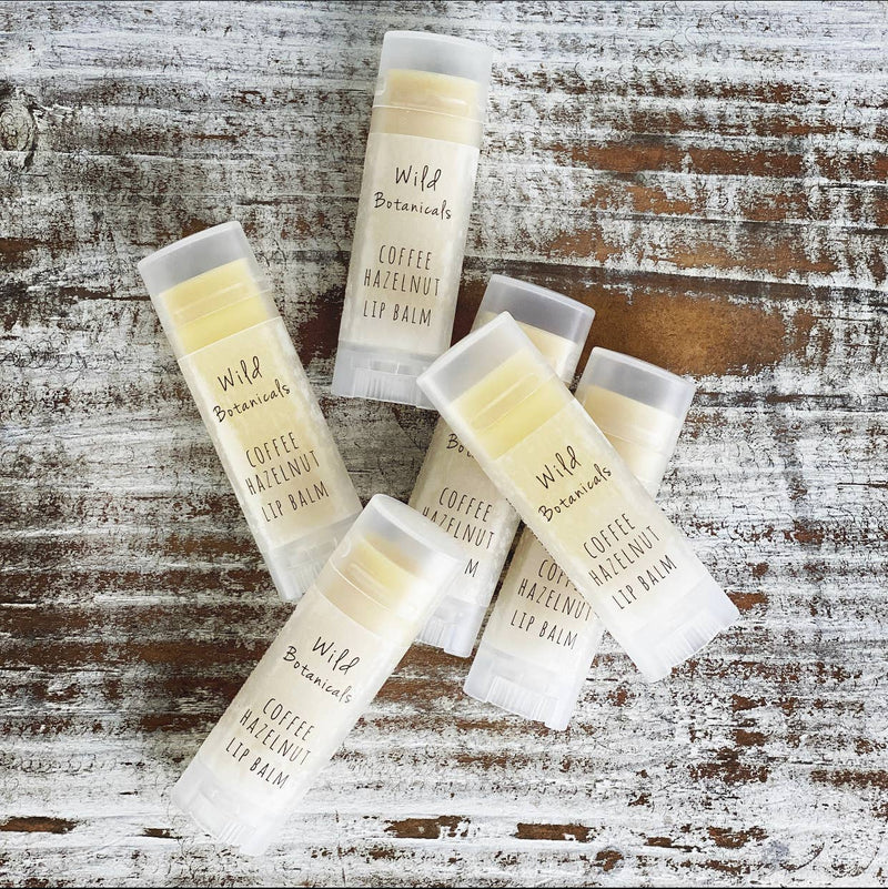 Flat lay of several tubes of Wild Botanicals - Coffee Hazelnut Lip Balm, handmade and enriched with Organic Jojoba Oil, arranged in a scattered fashion on a rustic wooden background.