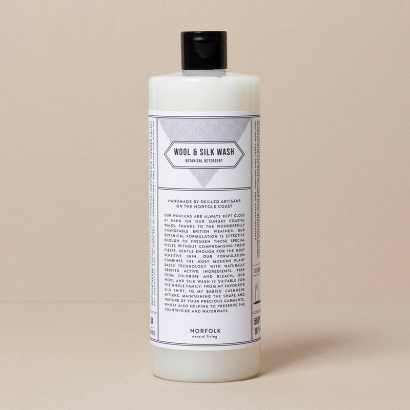 A white bottle of Norfolk Natural Living Coastal Wool and Silk Detergent with a black cap on a beige background. The label, featuring gentle formulation details, provides extensive product and usage information.