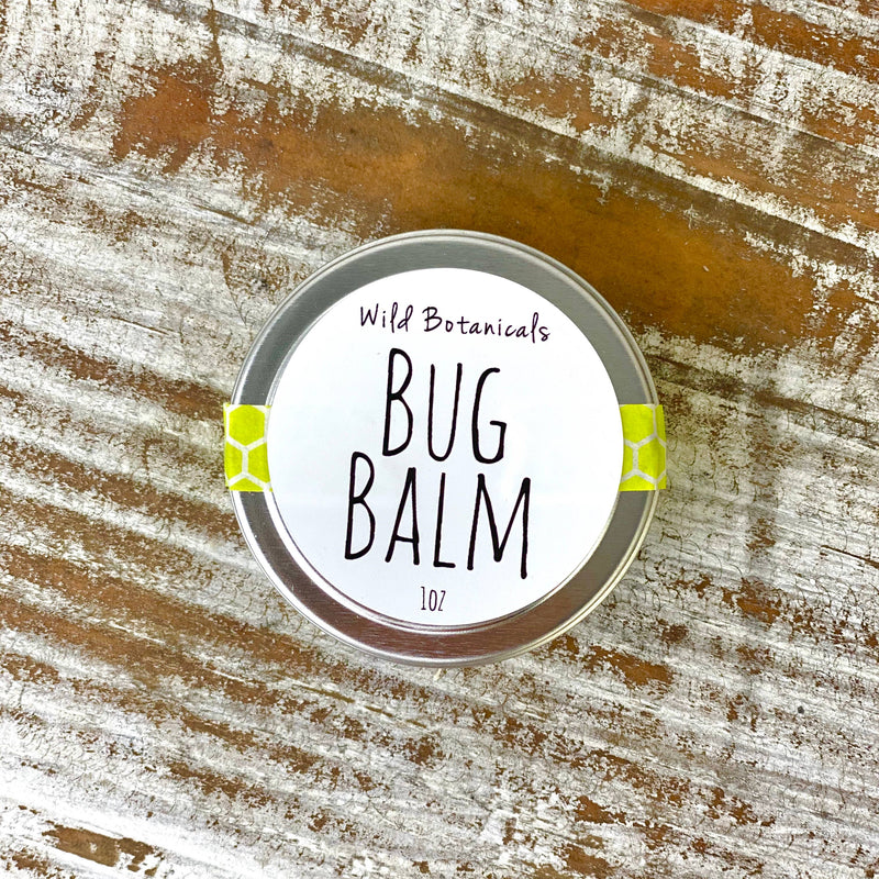 A small circular tin labeled "Wild Botanicals - 1oz Bug Off Balm" rests on a rustic wood surface, sealed with bright lime green tape on the sides.