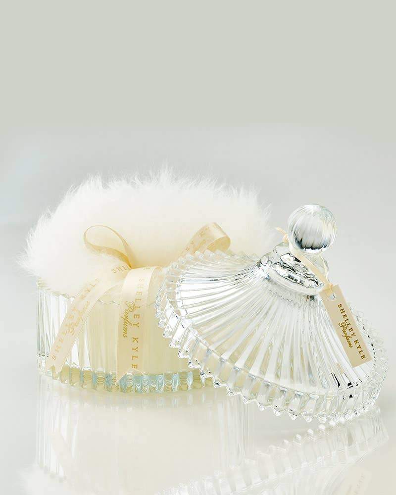A luxurious Large Crystal Puff Dish with a spherical stopper, accompanied by a fluffy white powder puff, on a reflective surface with a soft gray background by Odds & Ends.