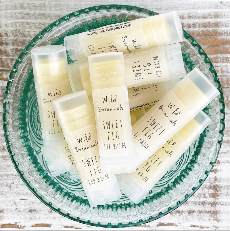 A collection of Wild Botanicals - Sweet Fig natural lip balm displayed in a circular green glass dish on a wooden background.