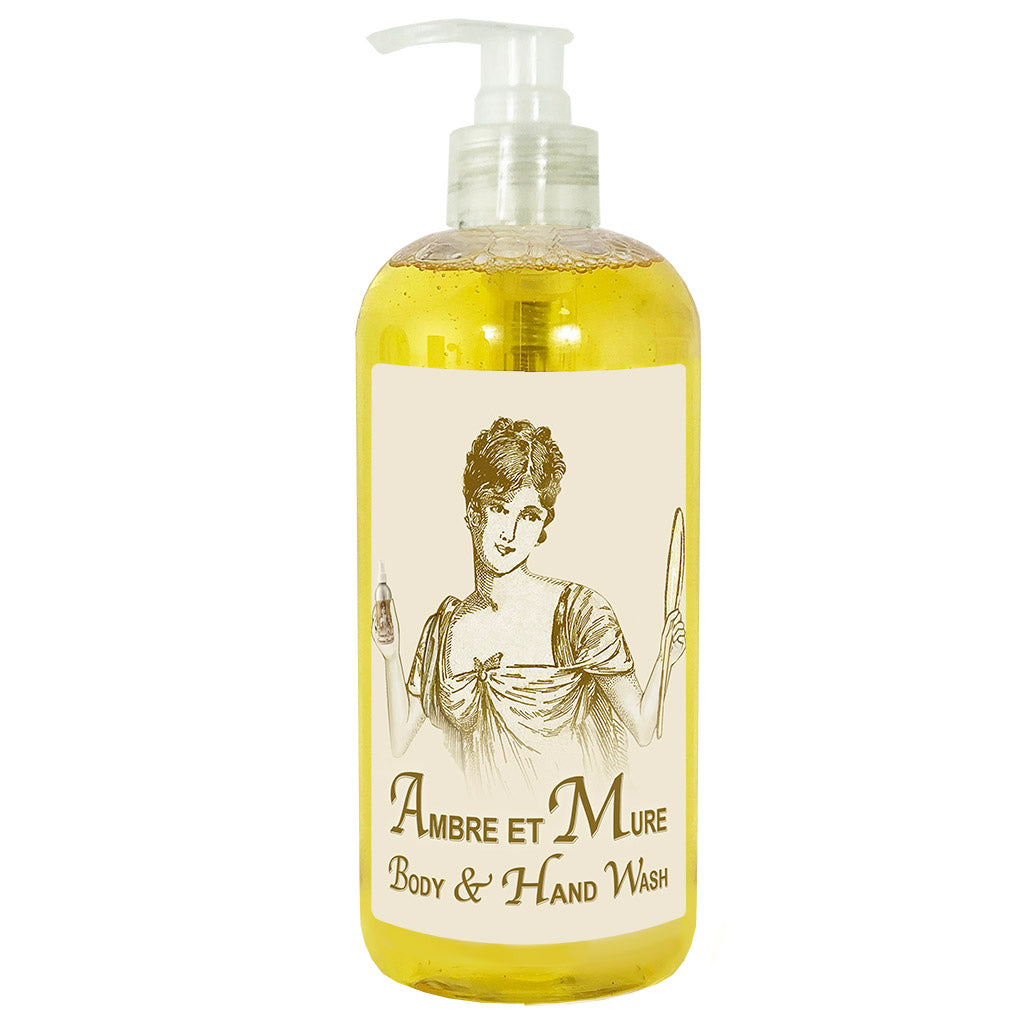 A clear pump bottle of "La Bouquetiere Ambre et Mure Gentle Hand & Body Wash" with a vintage-style illustration of a woman holding a feather and a mirror on the label. The liquid inside is yellow.