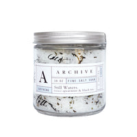 A Margot Elena glass jar of ARCHIVE Still Waters Salt Soak labeled "16 oz, Spearmint & Black Tea." The jar reveals visible salt crystals and purifying minerals with a clean, minimalist design.