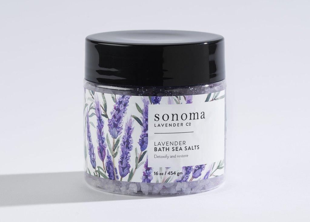 A jar of Sonoma Lavender Sea Salt Bath with a floral design on the label, containing purple salts, set against a white background.