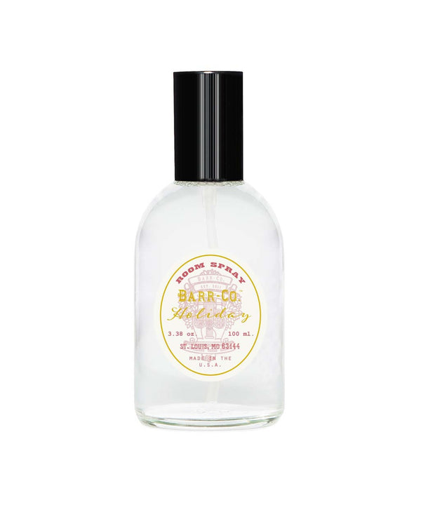 A clear glass bottle of Barr-Co. Holiday Room Spray against a white background, displaying a yellow and white label with black and gold text.