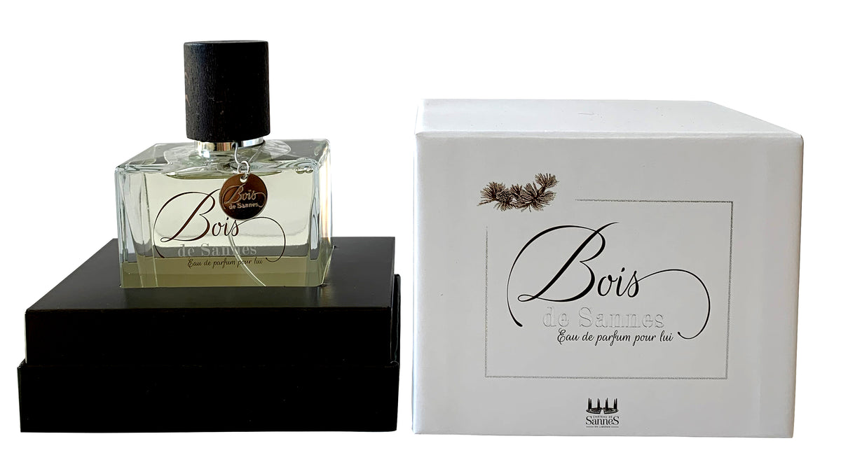 A bottle of Chateau De Sannes - Bois de Sannes eau de parfum rests beside its white packaging box, both adorned with elegant black text and subtle decorative elements.