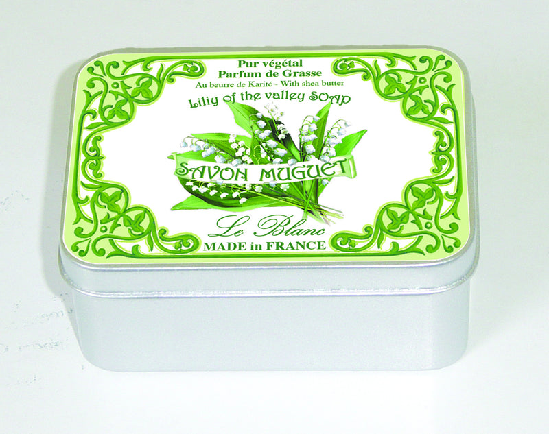 A decorative metal tin with a green and white floral design, labeled "Le Blanc Lily of the Valley 100gm Soap Tin," indicating it is made in France by Le Blanc Made in France perfumers and contains