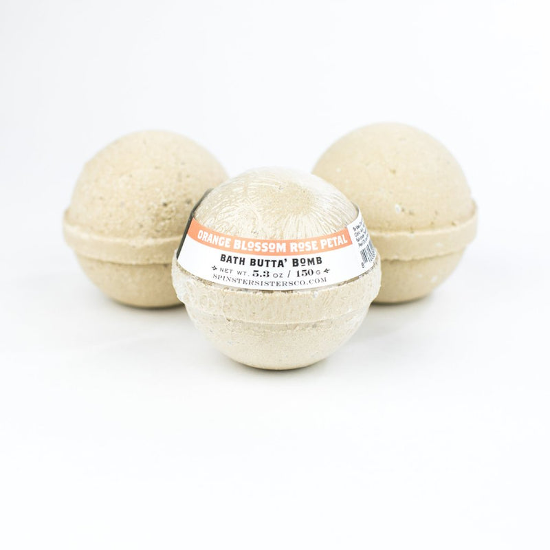 Three beige Spinster Sisters Bath Butta' Bombs enriched with shea butter, with a label on the front bath bomb reading "orange blossom rose petal bath butter bomb," displayed against a white background.