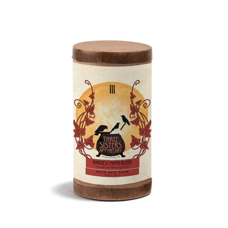 A cylindrical Three Sisters Apothecary Harvest Moon Bath Salt Soak container labeled with vintage-style graphics featuring essential oils and botanicals on a white background.