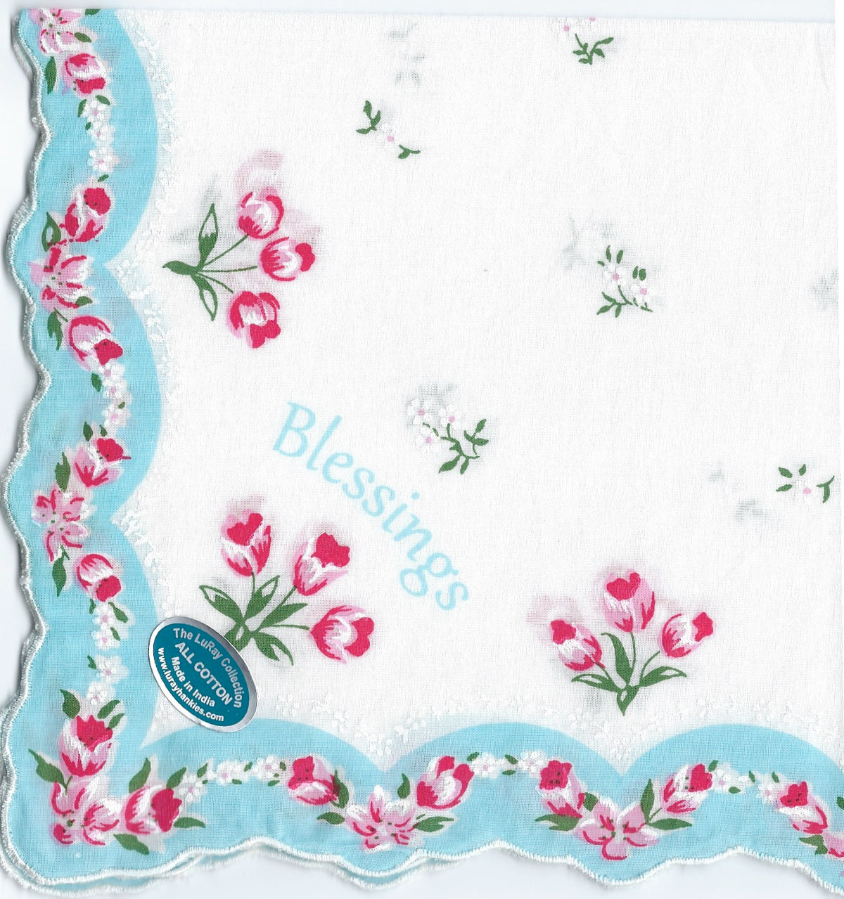 A decorative hanky with floral patterns and the word "blessings" in blue, framed by pink flowers and light green leaves on a white background, featuring a blue scalloped edge, crafted by Hankies ala Carte.