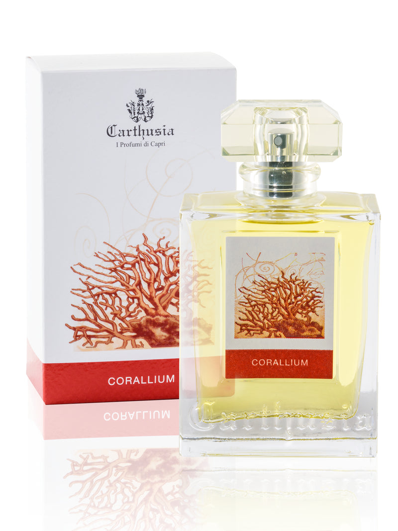 A bottle of Carthusia I Profumi de Capri Corallium Eau de Parfum 50ml next to its box. The glass bottle is square with a beige label decorated with red coral, holding yellow liquid. The box features a white background and