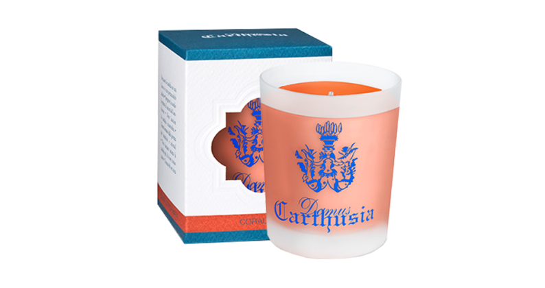 A Carthusia Corallium Candle with an orange wax and a blue crest printed on it, next to its white and blue packaging box with matching design elements.