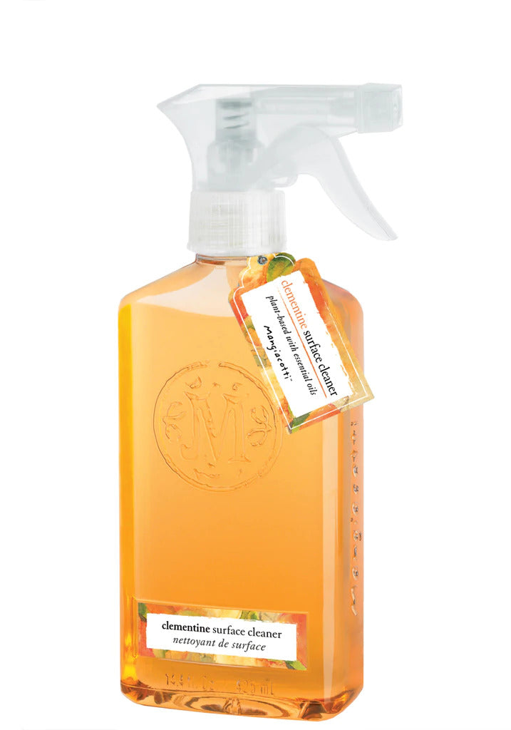 A transparent spray bottle containing orange liquid, labeled "Mangiacotti Clementine Surface Cleaner" with a small, dangling tag that provides additional product information.