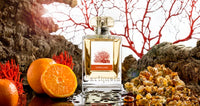 A perfume bottle labeled "Carthusia Corallium Eau de Parfum - 100ml" by Carthusia I Profumi de Capri is centered between coral-like textures and vivid orange accents, with slices of oranges to its left and amber-colored crystals to its right, highlighted.
