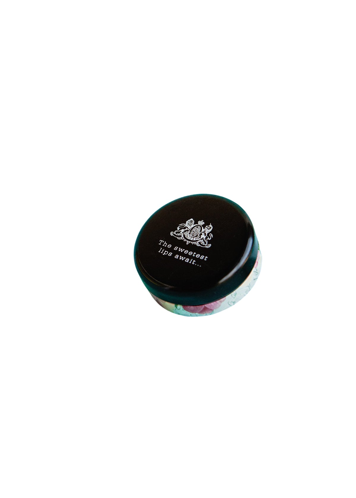 A small, circular tin lip balm container, predominantly black, labeled "TokyoMilk Dead Sexy Lip Balm." The container rests on a plain white background. Brand Name: Margot Elena