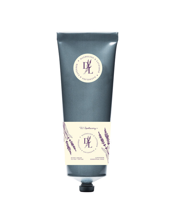 A tube of U.S. Apothecary Dandelion & Lavender Hand & Body Cream, presented on a plain background. The tube is colored in a muted blue with a decorative lavender-themed label in shades of cream and purple. This moisturizing she