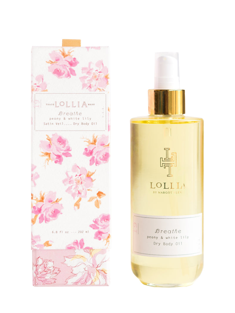 A bottle of Margot Elena's Lollia Breathe Dry Body Oil, enriched with hydrating coconut and sweet almond oils, next to its floral-patterned packaging. The packaging features pink flowers on a