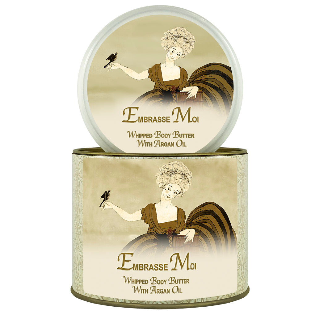 An image showcasing two cylindrical containers of La Bouquetiere Embrasse Moi Argan Oil Whipped Body Butter. One container is open, displaying the product, and both feature an elegant vintage-style illustration of a woman holding.