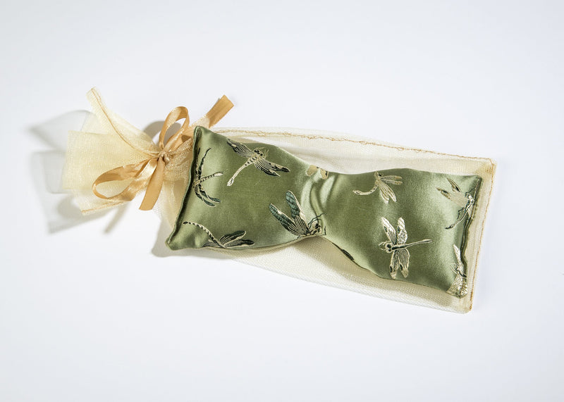 A Sonoma Lavender green satin eye mask with embroidered dragonfly patterns and flaxseed filling, tied with a delicate gold ribbon, displayed on a bright, white background.