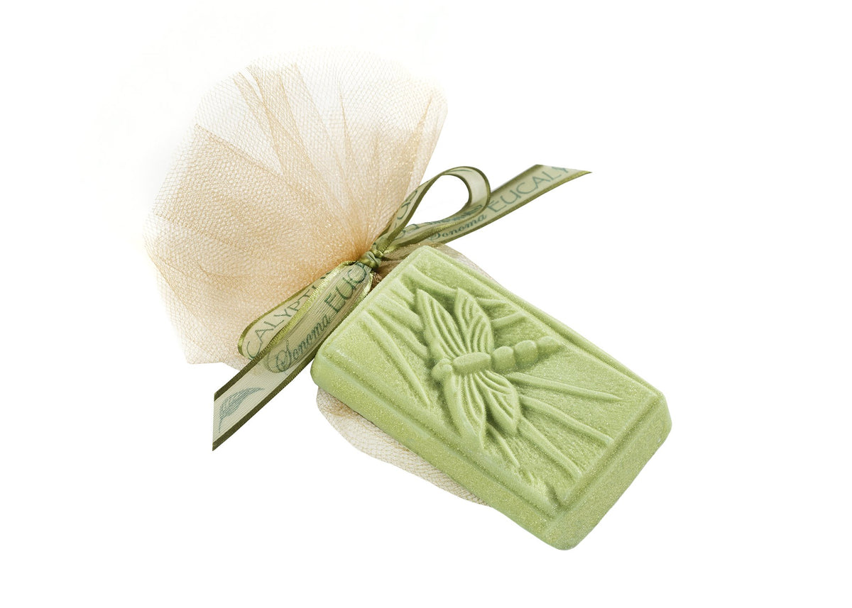 A green Sonoma Eucalyptus Oil Dragonfly soap bar with a textured design, wrapped in a light beige mesh cloth and tied with a green ribbon labeled "eucalyptus.