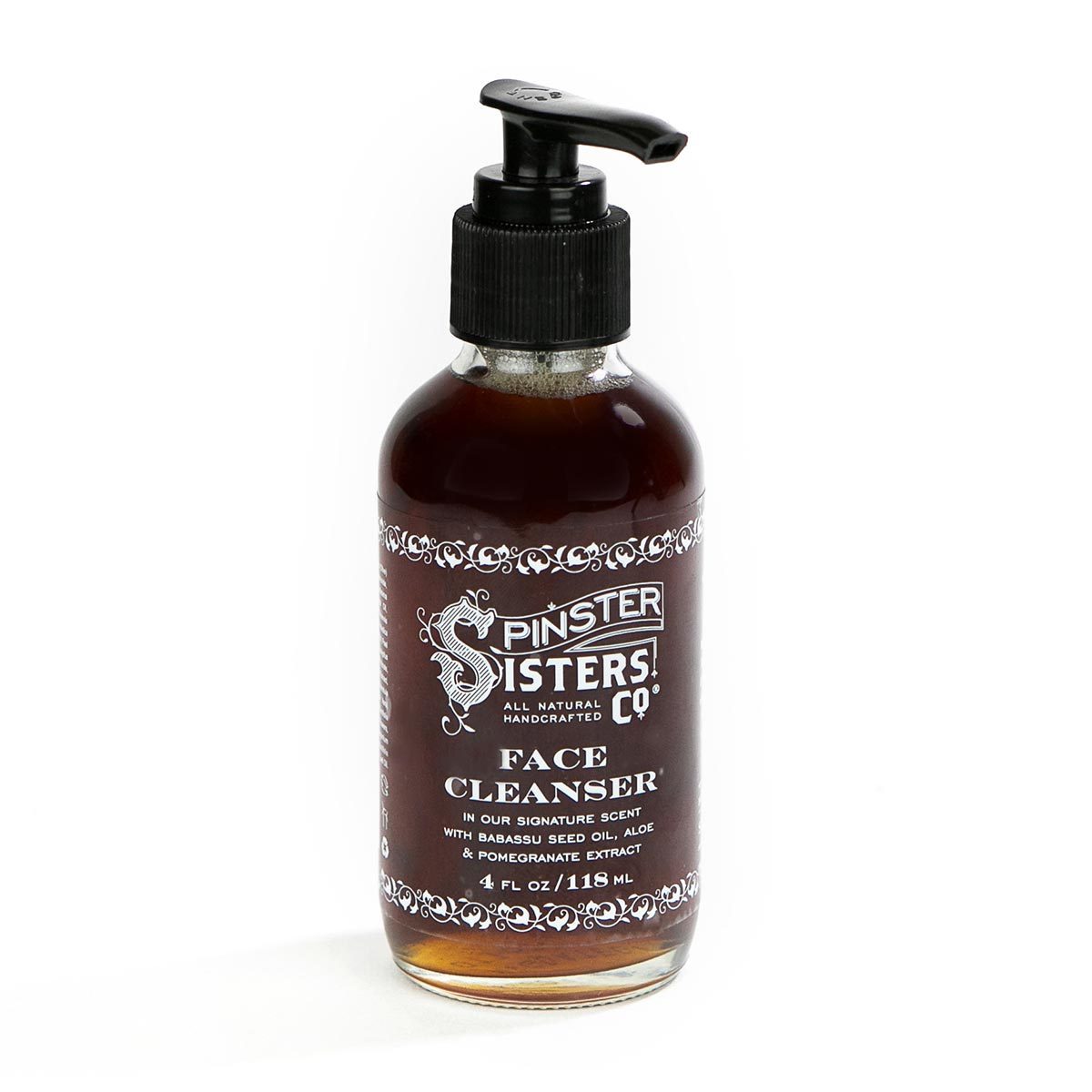 Sentence with replacements: Amber glass bottle with a black pump, labeled "Spinster Sisters Co. Spinster Sisters Face Cleanser" with ornate designs and product details, isolated on a white background.