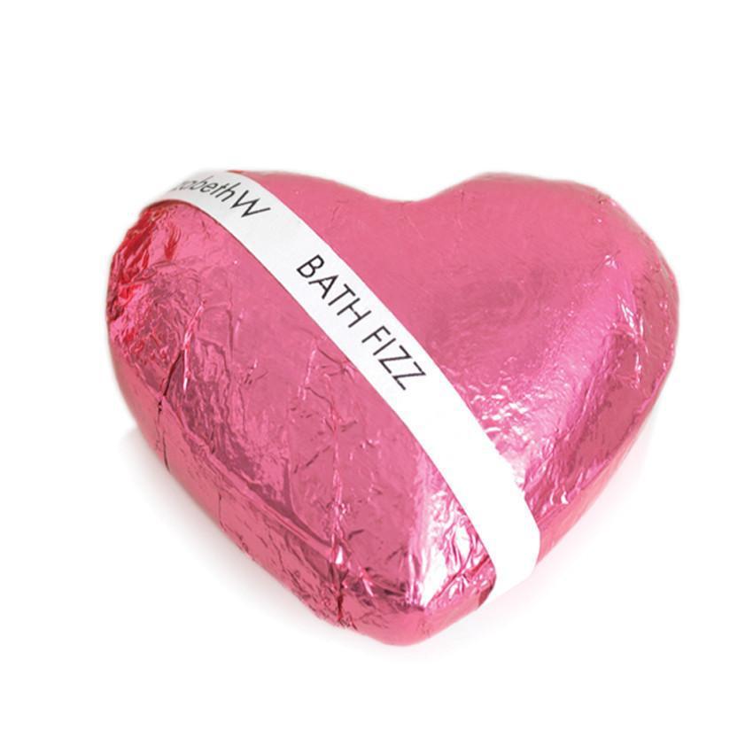 A pink, heart-shaped bath bomb wrapped in metallic pink foil with a white label that reads "elizabeth W Lavender Fizz Heart." It's isolated on a white background.