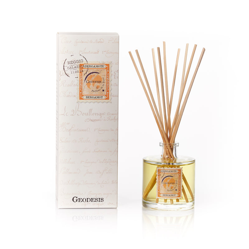 A Geodesis Bergamot Reed Ambiance Diffuser in a clear glass container labeled "Calabrian Treasure" with several brown reeds inserted, standing next to its product packaging with elegant text design.