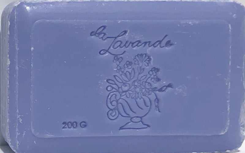 A La Lavande Lavender Blue Soap bar with the embossed inscription "la lavande" and a decorative floral design, featuring various flowers in a vase. The soap, infused with Shea Butter, weighs 200 grams.