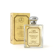 A bottle of Taylor of Old Bond Street Sandalwood Luxury Aftershave Lotion - 100ml next to its packaging. The bottle is clear with a silver cap and has a label in elegant script. The box is beige with ornate golden designs and text.