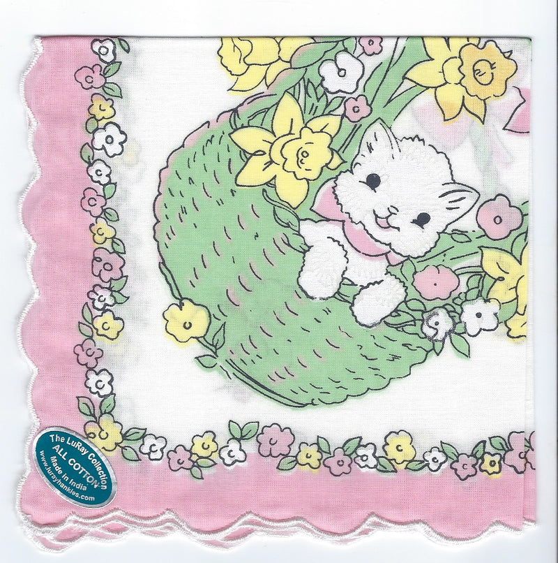 A Vintage-Inspired Hanky - White Kitty in Green Basket Hanky featuring a cute white kitten peeking out from a green woven basket, surrounded by yellow daffodils and small pink flowers, with a floral border from Hankies ala Carte.