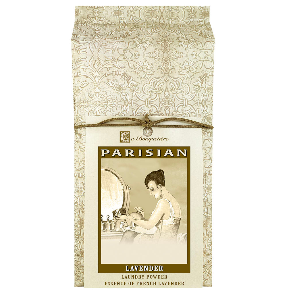 A package of La Bouquetiere Tendre est la Nuit laundry powder, featuring elegant, patterned design with an image of a woman at a vanity on the label. It's tied with a ribbon at the top and infused with Parisian lavender.