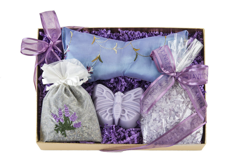 A Sonoma Lavender Sweet Dreams Kit containing a lavender eye pillow, two sachets filled with dried lavender, a butterfly ornament, and lavender-scented bath salts, all on a bed of purple shredded paper.