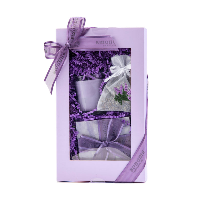 A Sonoma Lavender - Lavender Treatment Gift Set displayed in a windowed box, featuring a mug, candles, bath items including lavender essential oil, and adorned with a matching ribbon.