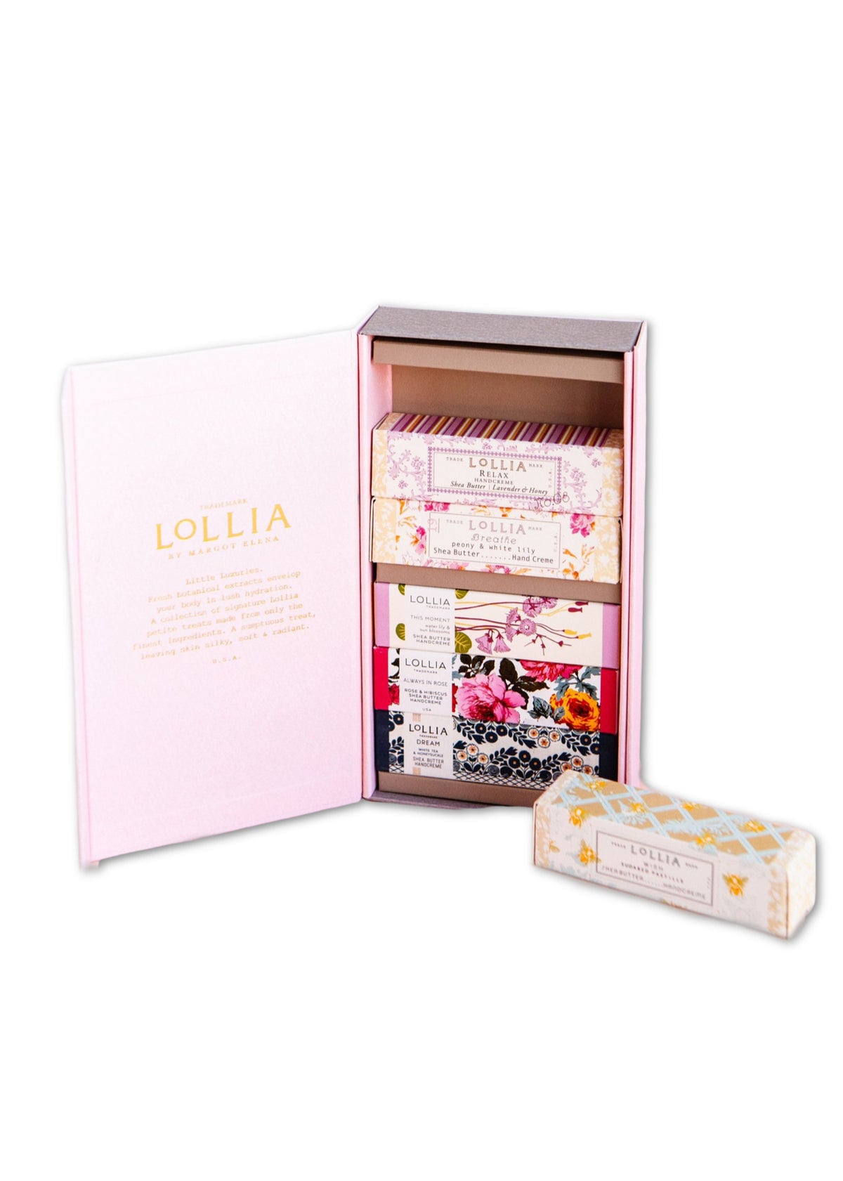 A Margot Elena Lollia Petite Treat Handcreme Gift Set opens to reveal a collection of bath products, including soap bars and hand cream, each decorated with floral designs, against a pastel pink background.
