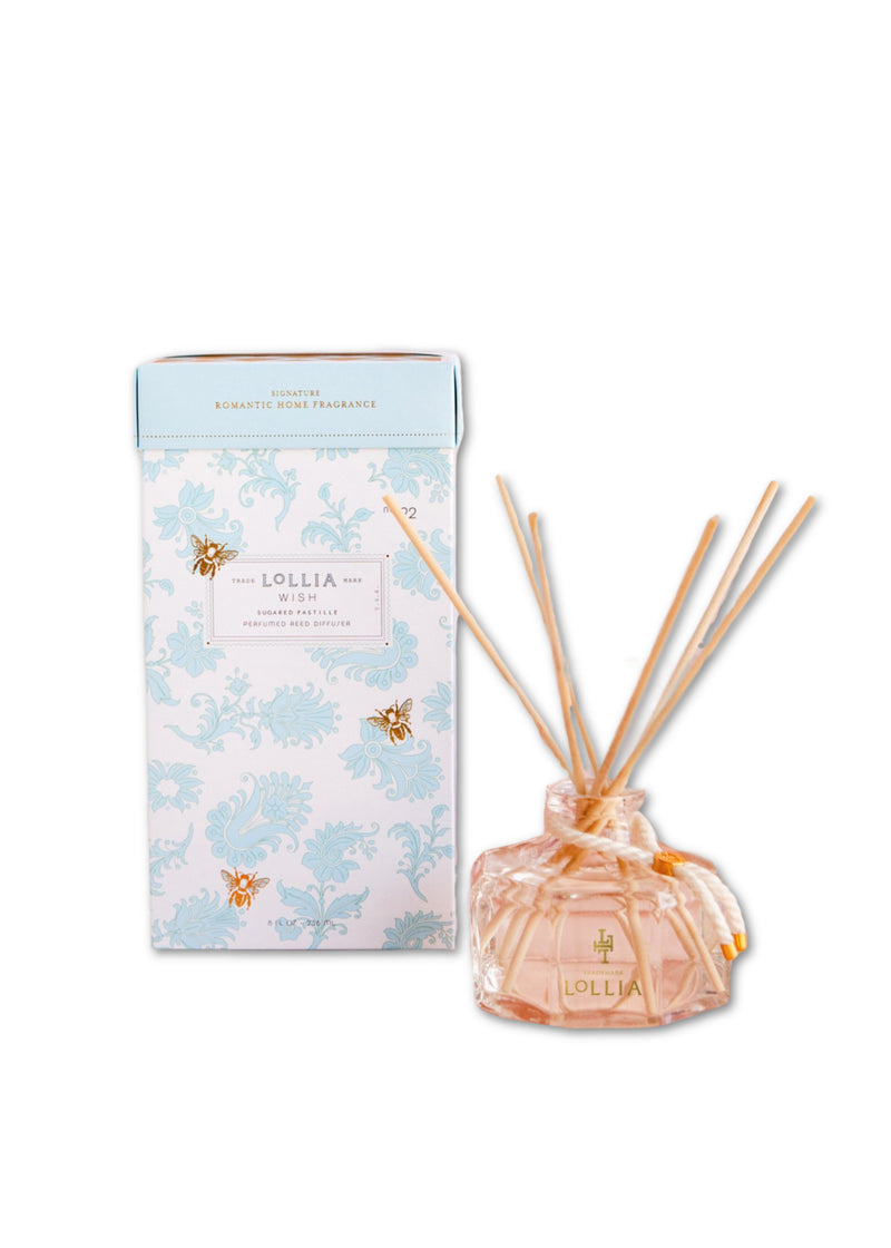 A Lollia Wish Perfumed Reed Diffuser set by Margot Elena featuring fragrance reeds in a decorative glass bottle with pink liquid scented with jasmine and vanilla bean, alongside a light blue and white patterned box labeled "lollia.