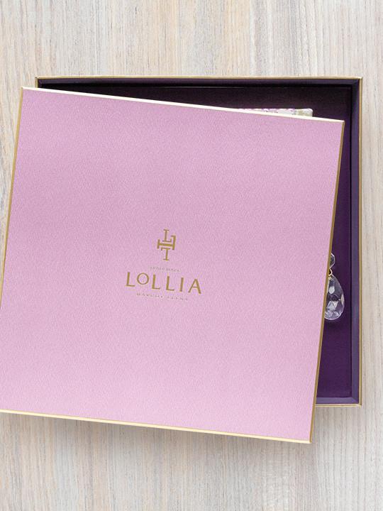 A pink Margot Elena Lollia Relax Gift Set with a shiny logo, slightly open to reveal a dark purple interior and a glimpse of an enclosed item with a crystal charm.