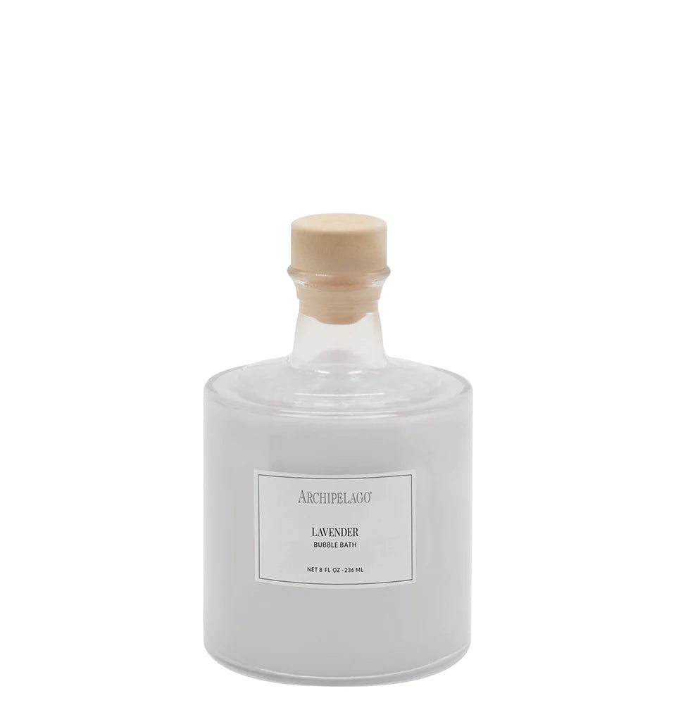 A clear glass bottle with a wooden cork stopper, labeled "Archipelago Botanicals Lavender Bubble Bath," containing a milky white liquid, against a white background.