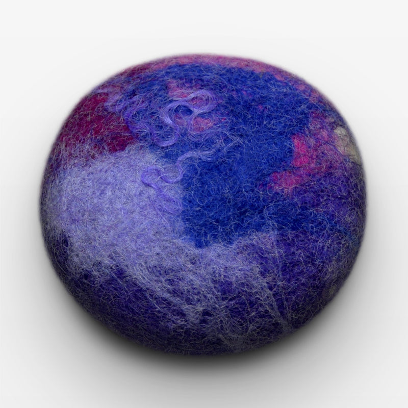A close-up image of a round, Fiat Luxe - Classic Lavender felted soap with a textured surface in shades of blue, purple, and pink, resembling a small planet.