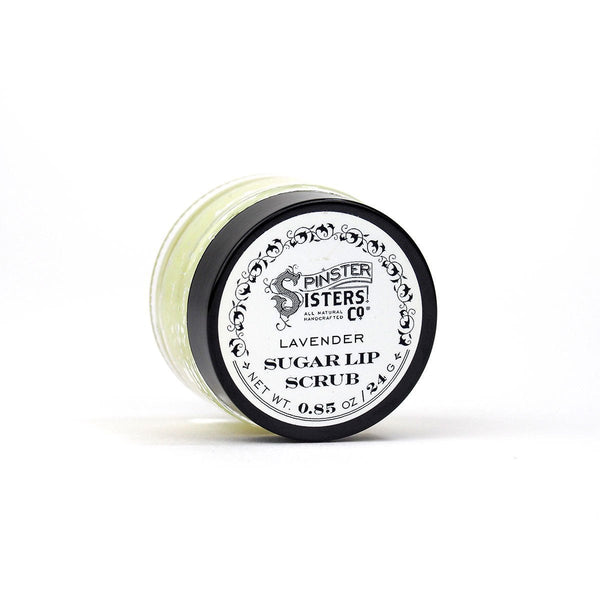 A small jar of Spinster Sisters, Co. Lavender Sugar Lip Scrub, containing 0.85 oz (24 g). The jar has a black lid and a white label with ornate black detailing and text describing the product. This hydrating sugar-based scrub appears to be light green in color.