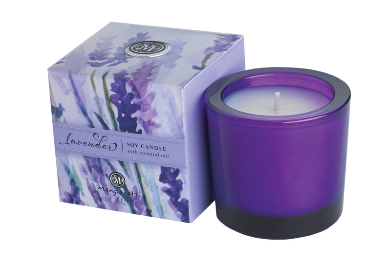 A Mangiacotti lavender-scented soy aromatherapeutic candle in a purple glass with a matching box labeled "French lavender," featuring an image of purple lavender fields. The box notes it includes essential oils.