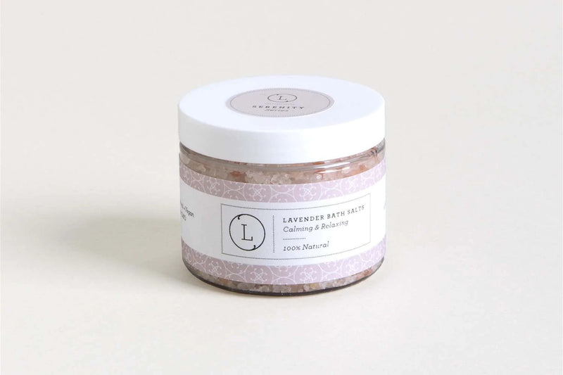A clear jar of Lizush Lavender Bath Salt Soak with Dead sea, Epsom and Himalayan salts labeled "lavender bath salts, calming & relaxing, 100% natural" on a light beige background.