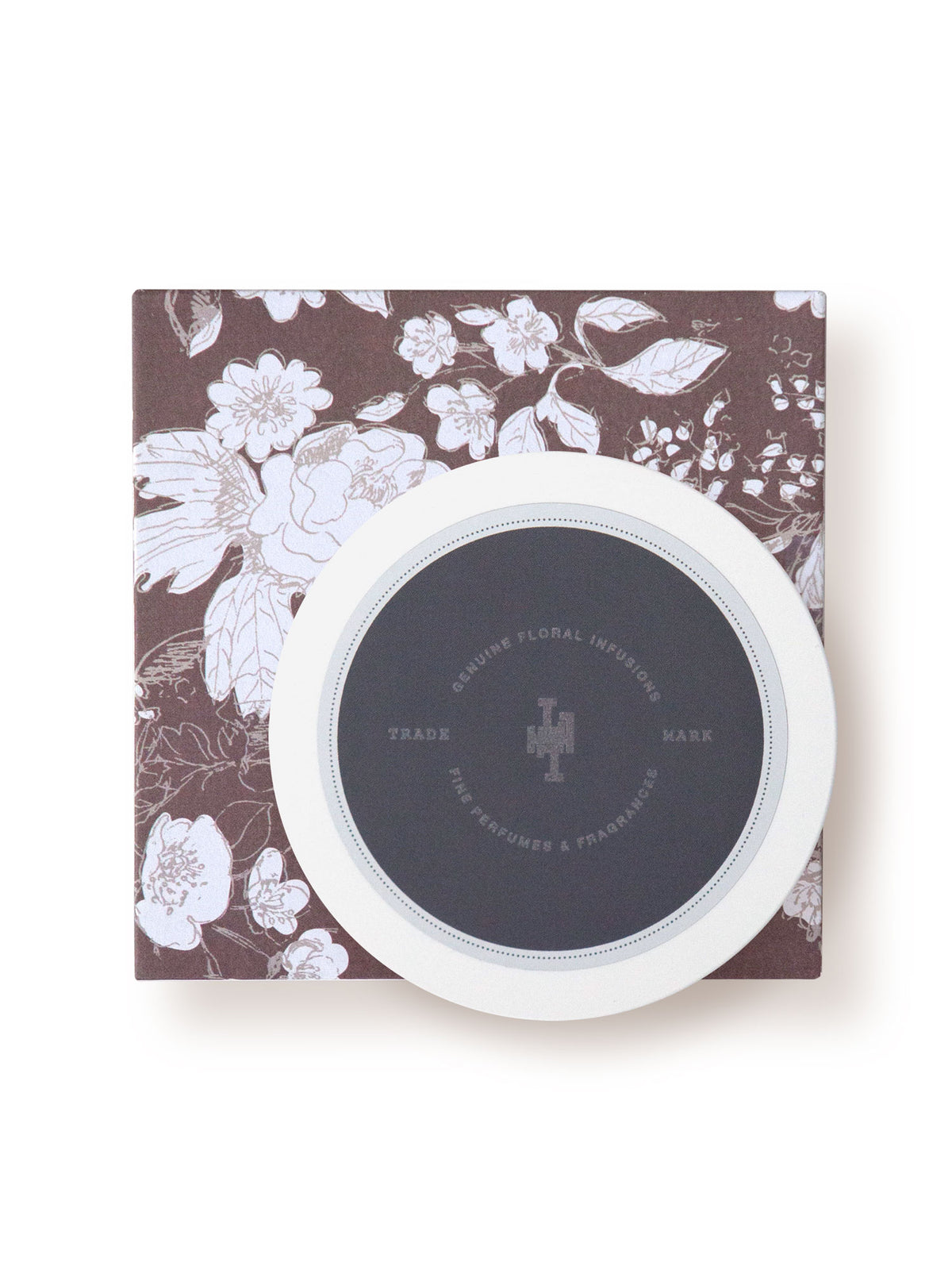 A round, white Margot Elena compact with a cocoa butter scent and a floral design on the case, placed on a matching floral box against a plain background. The compact features a logo in the center.