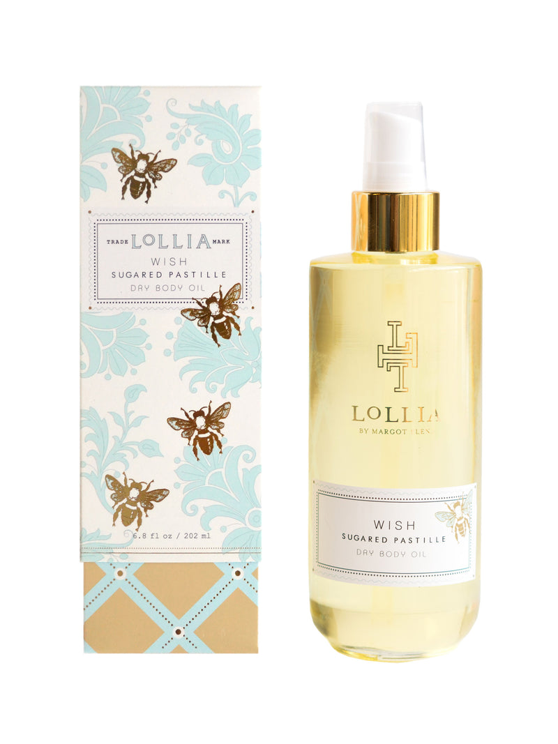 A bottle of Margot Elena Lollia Wish Dry Oil Body next to its packaging, formulated with hydrating coconut and sweet almond oil. The bottle is transparent with gold liquid and a spray nozzle. The packaging