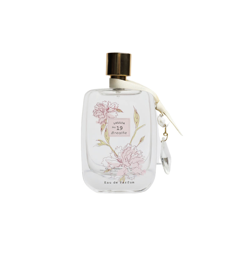 A clear perfume bottle with a golden cap and an attached golden charm, featuring elegant floral designs including white lily and peony, and the words "Lollia Breathe Eau de Parfum" by Margot Elena on.