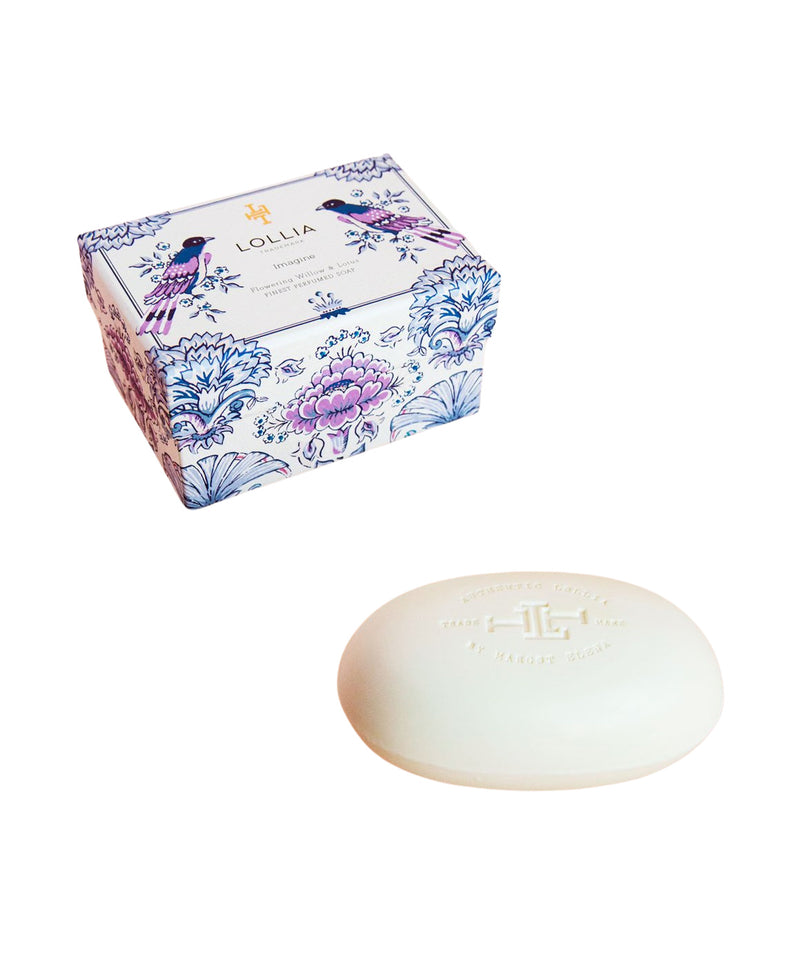 A bar of Margot Elena's Lollia Imagine Shea Butter Soap lying in front of its floral printed packaging box labeled "lollia" with the scent "Flowering Willow & Lotus." The soap has an embossed logo and text.