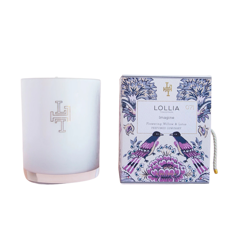 A Margot Elena brand Lollia Imagine No. 71 Perfumed Luminary Candle in a translucent white holder with an "lh" monogram, next to its packaging box adorned with a floral and bird design, and featuring the scent of Flower.