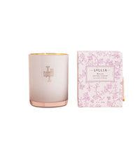 A pink Lollia Relax No. 08 Luminary Candle made from a soy wax coconut wax blend, with a gold monogram next to its matching floral-patterned boxed packaging, both labeled "Margot Elena" and "breat".