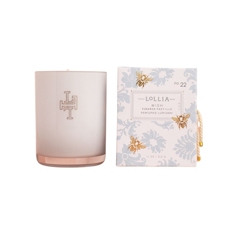 A pink handblown glass Lollia Wish No. 22 Luminary Candle with a monogram and a box of floral-patterned Margot Elena perfumed laundry wash, both set against a white background.