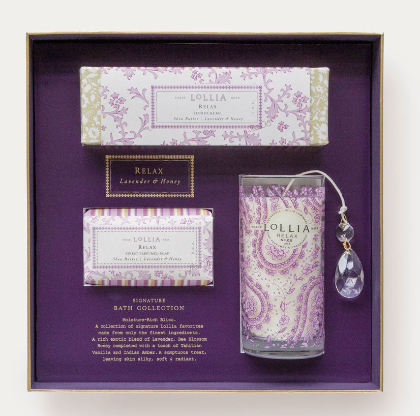 A gift box containing Margot Elena's Lollia Relax Gift Set including a Bee Blossom Honey bar soap, shea butter hand cream, and a floral bath salt tube with a hanging crystal charm.